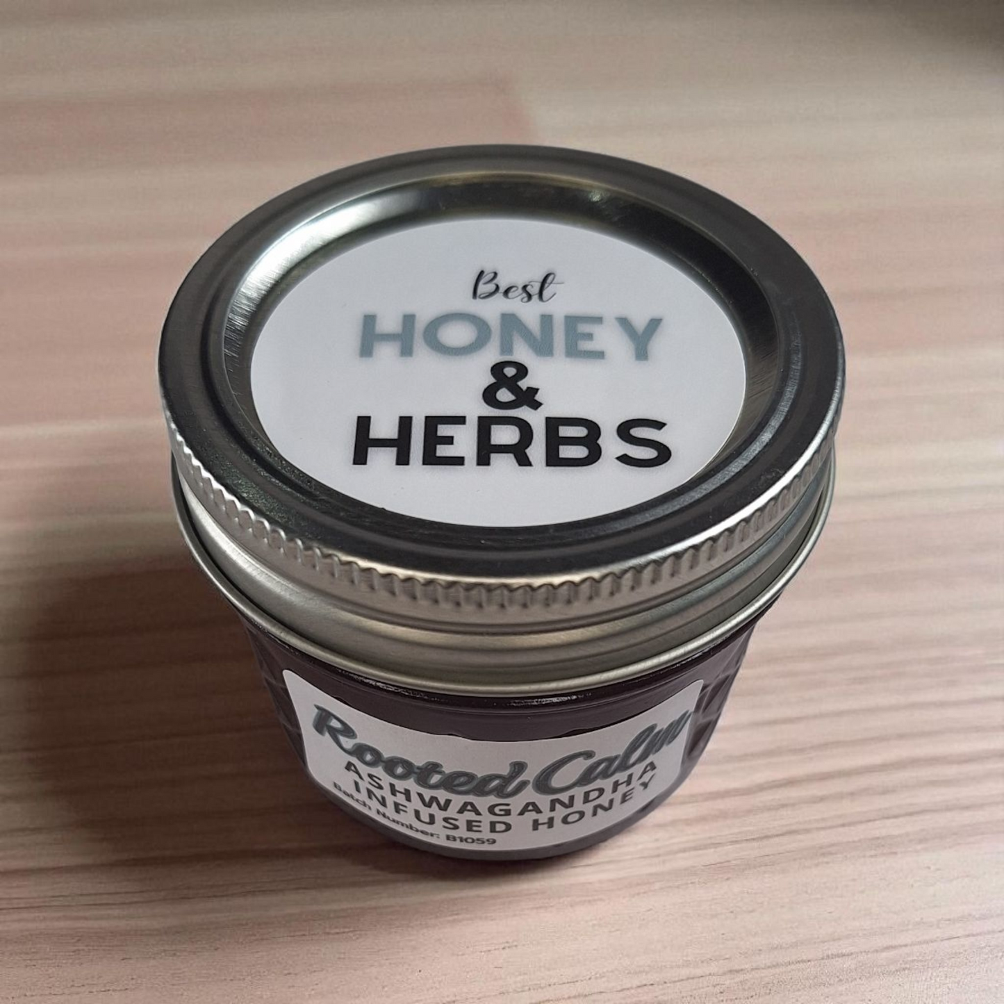 Overhead close-up of a 4 oz quarter-pint jar of raw Ashwagandha Infused Honey on warm wood grain; small-batch herbal sweetener ideal for evening tea and baked goods.