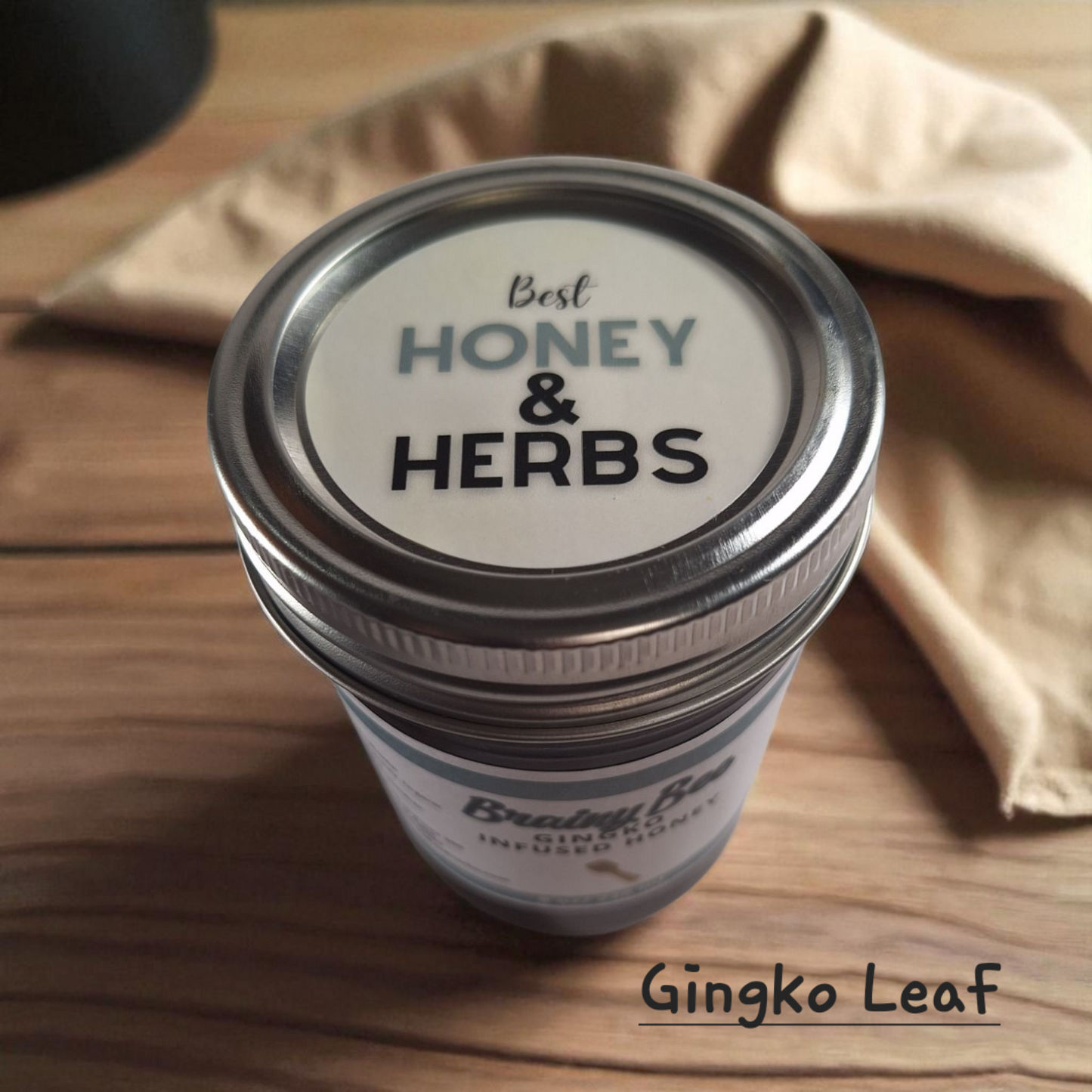 Top view of 8 oz half-pint jar of raw Ginkgo Infused Honey on a wooden surface, herbal honey for tea, memory support, and healthy recipes.