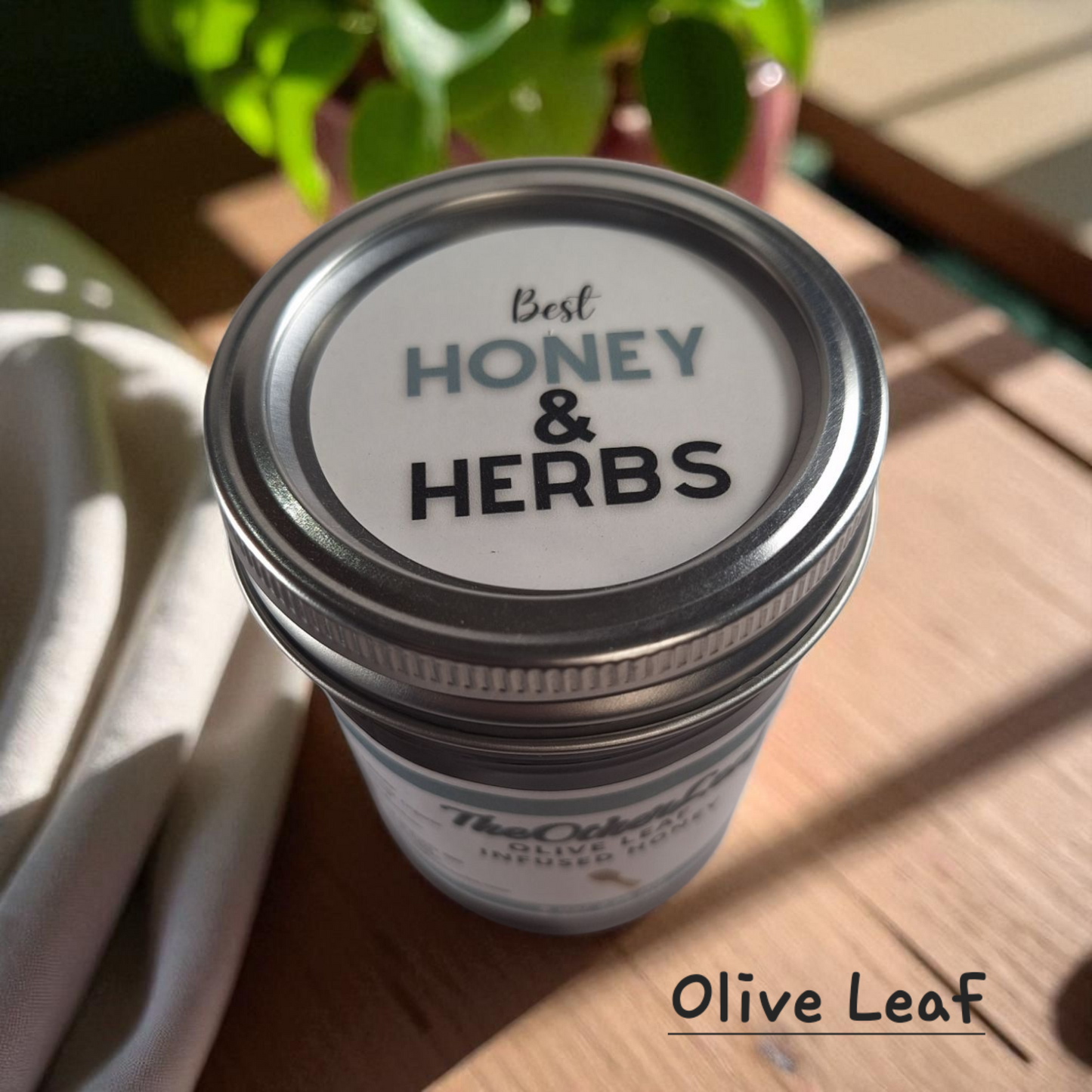 Top view of 8 oz half-pint jar of raw Olive Leaf Infused Honey on a rustic wooden surface, herbal sweetener for tea, wellness tonics, and healthy recipes.