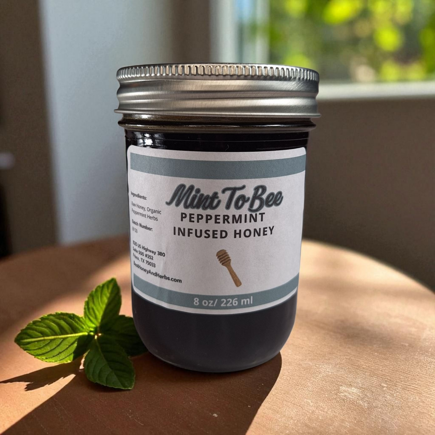 8 oz half-pint jar of raw Peppermint Leaf Infused Honey on a wooden surface, refreshing herbal sweetener for tea, baking, and holiday treats.