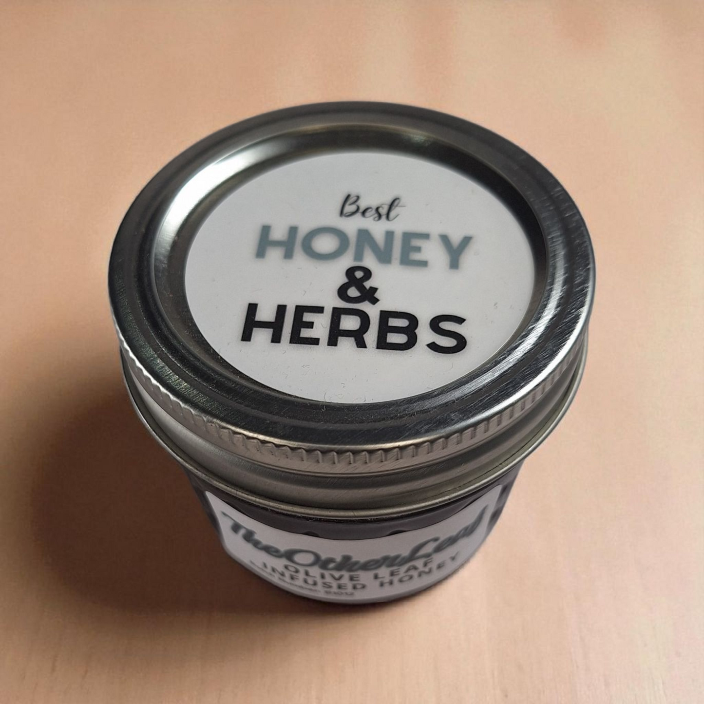 Overhead 4 oz Olive Leaf Infused Honey on deep wood grain; nuanced herbal honey for herbal tonics and drizzle over cheese.