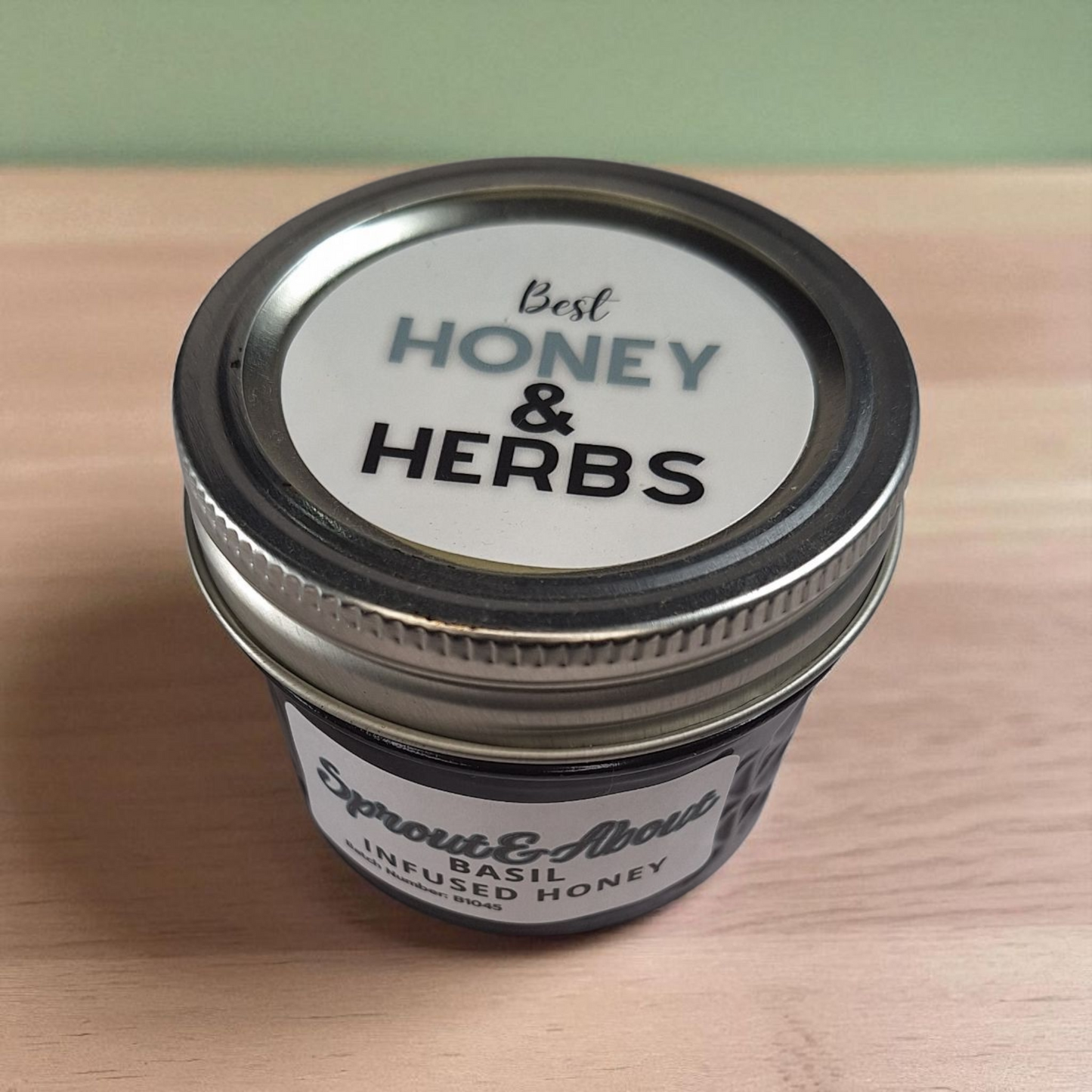 Top-down shot of 4 oz Basil Infused Honey on a wooden board; artisan herbal honey for cheese boards, caprese salads, and crusty bread.