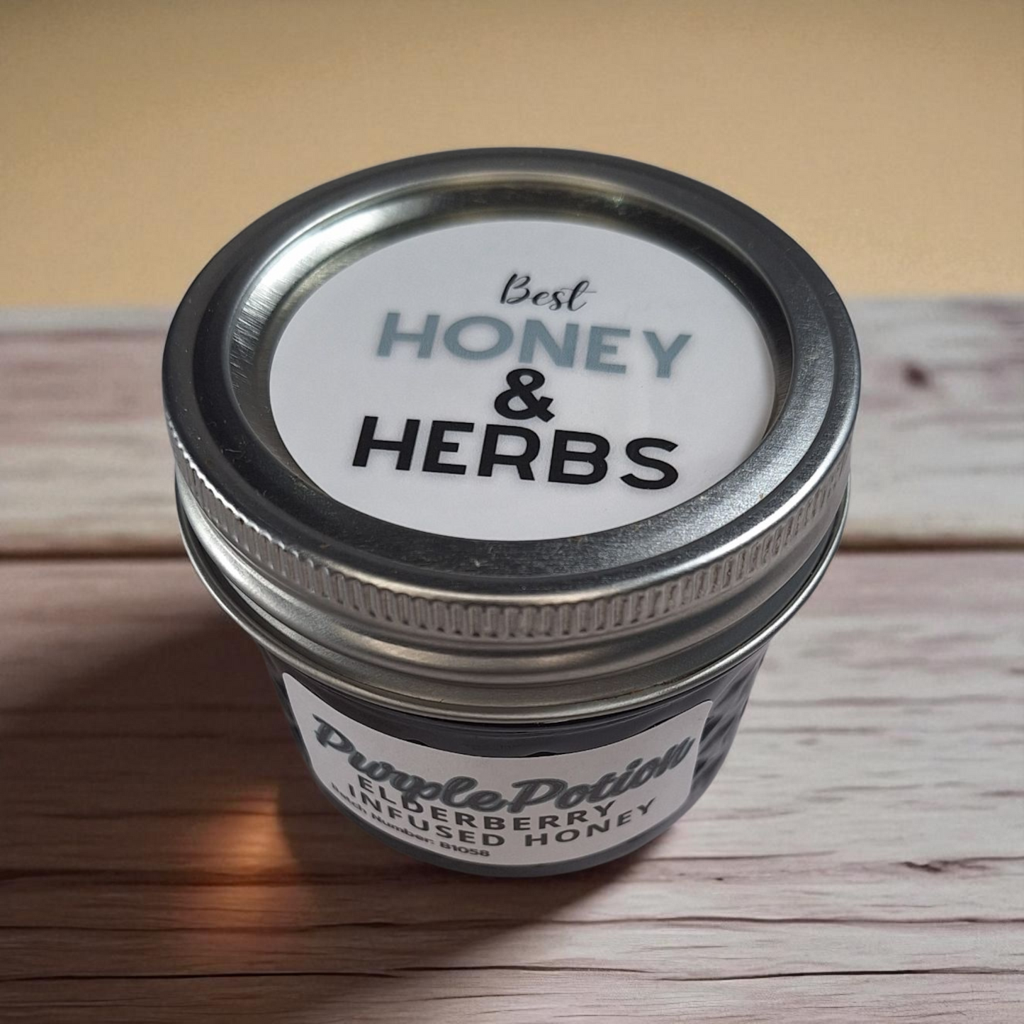 Overhead 4 oz Elderberry Infused Honey on dark wood; rich, fruity herbal honey for iced tea, yogurt bowls, and glazes.