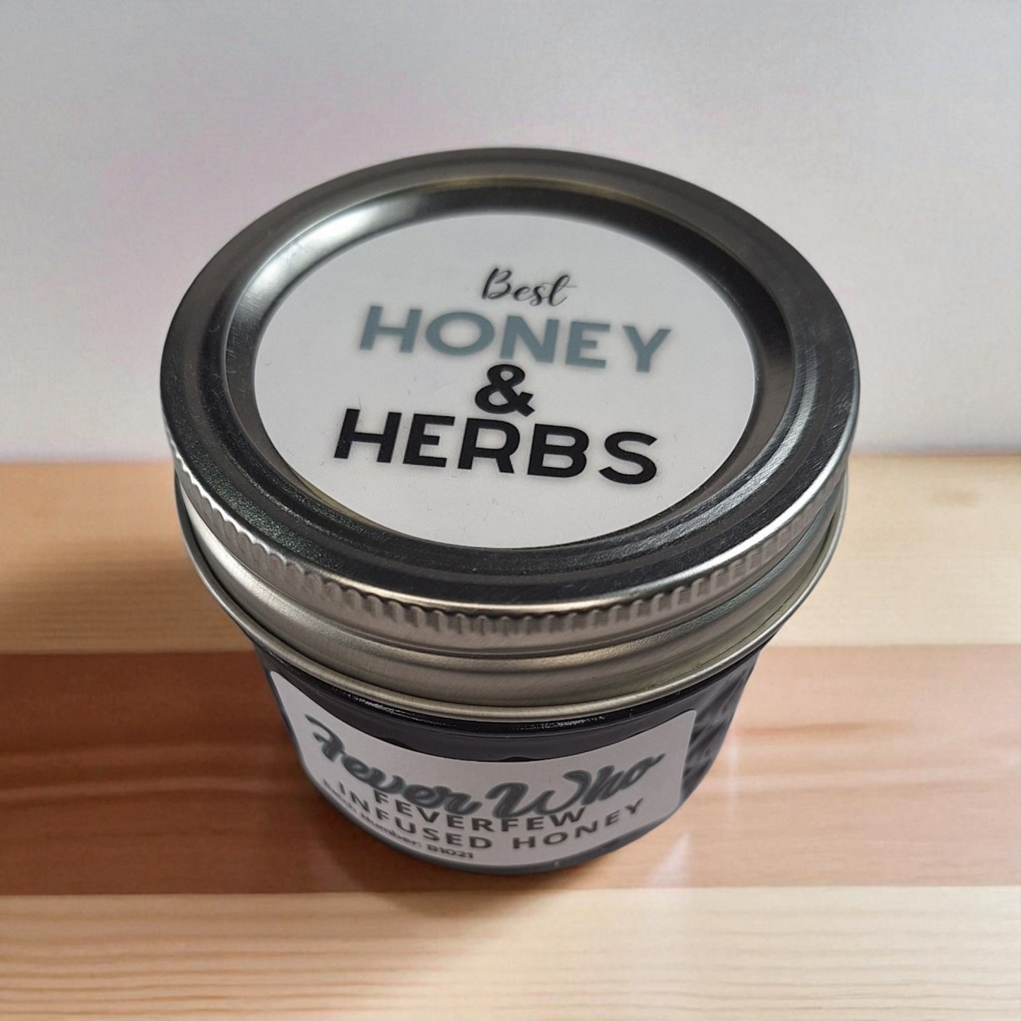 Top-down 4 oz jar of Feverfew Infused Honey on rustic wood; traditional herbal sweetener for warm teas and simple syrups.