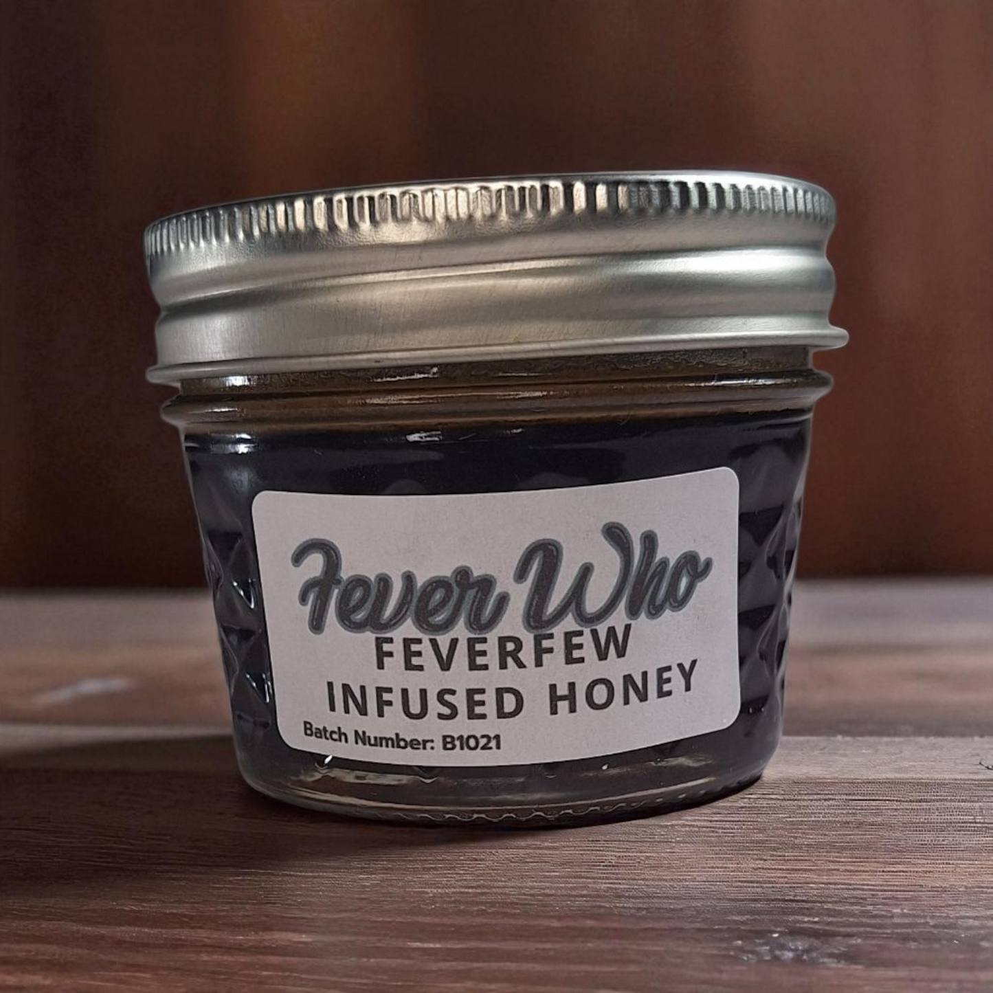 4 oz jar of raw Feverfew Infused Honey on a rustic wooden surface, herbal sweetener for tea, baking, and traditional herbal uses.