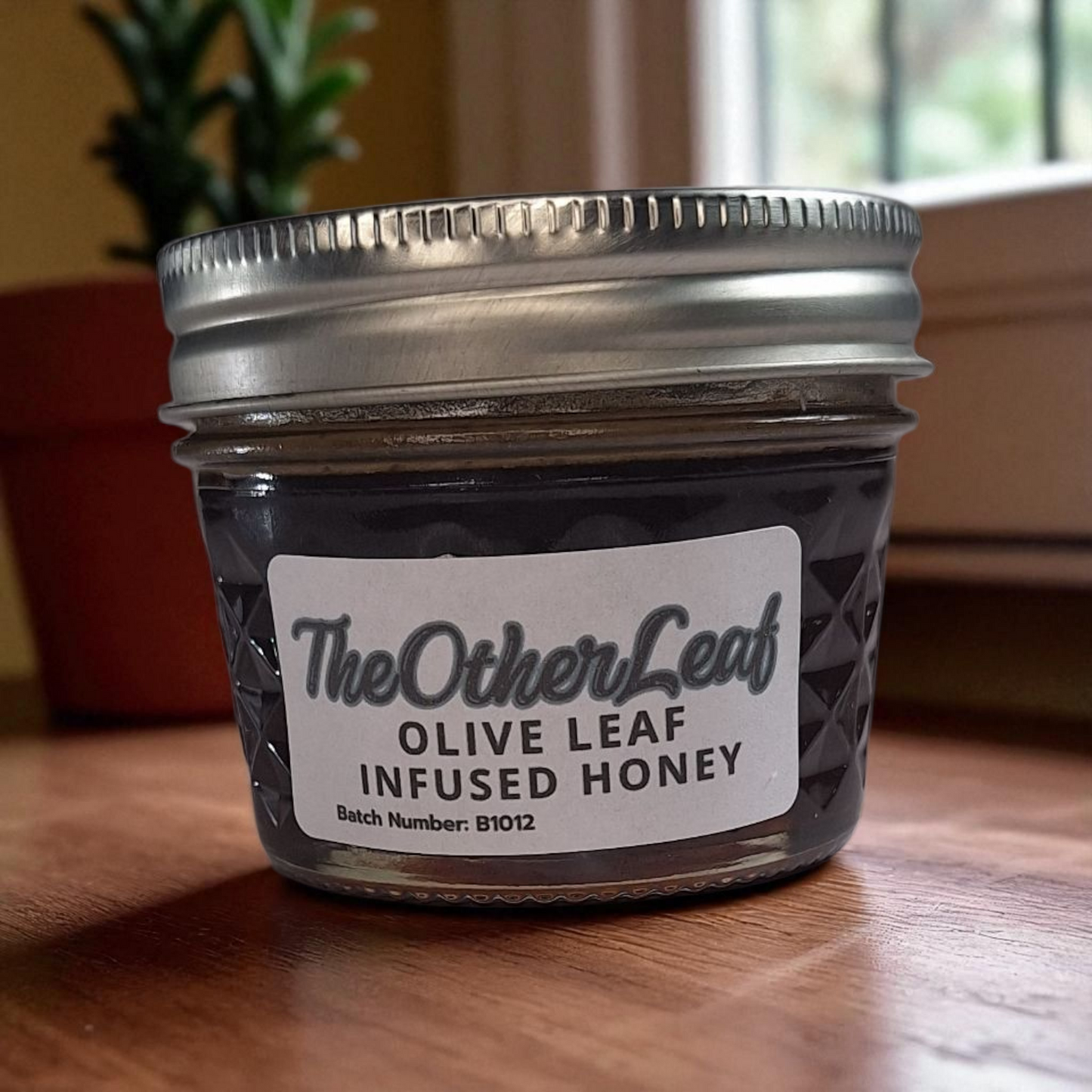 4 oz jar of raw Olive Leaf Infused Honey on a rustic wooden surface, herbal sweetener for tea, wellness tonics, and healthy recipes.