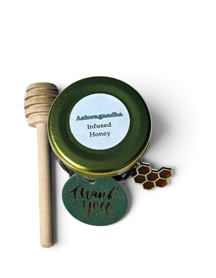A small round tin of Ashwagandha Infused Honey with a wooden honey dipper, a green 'Thank You' tag, and a small honeycomb charm on a white background.