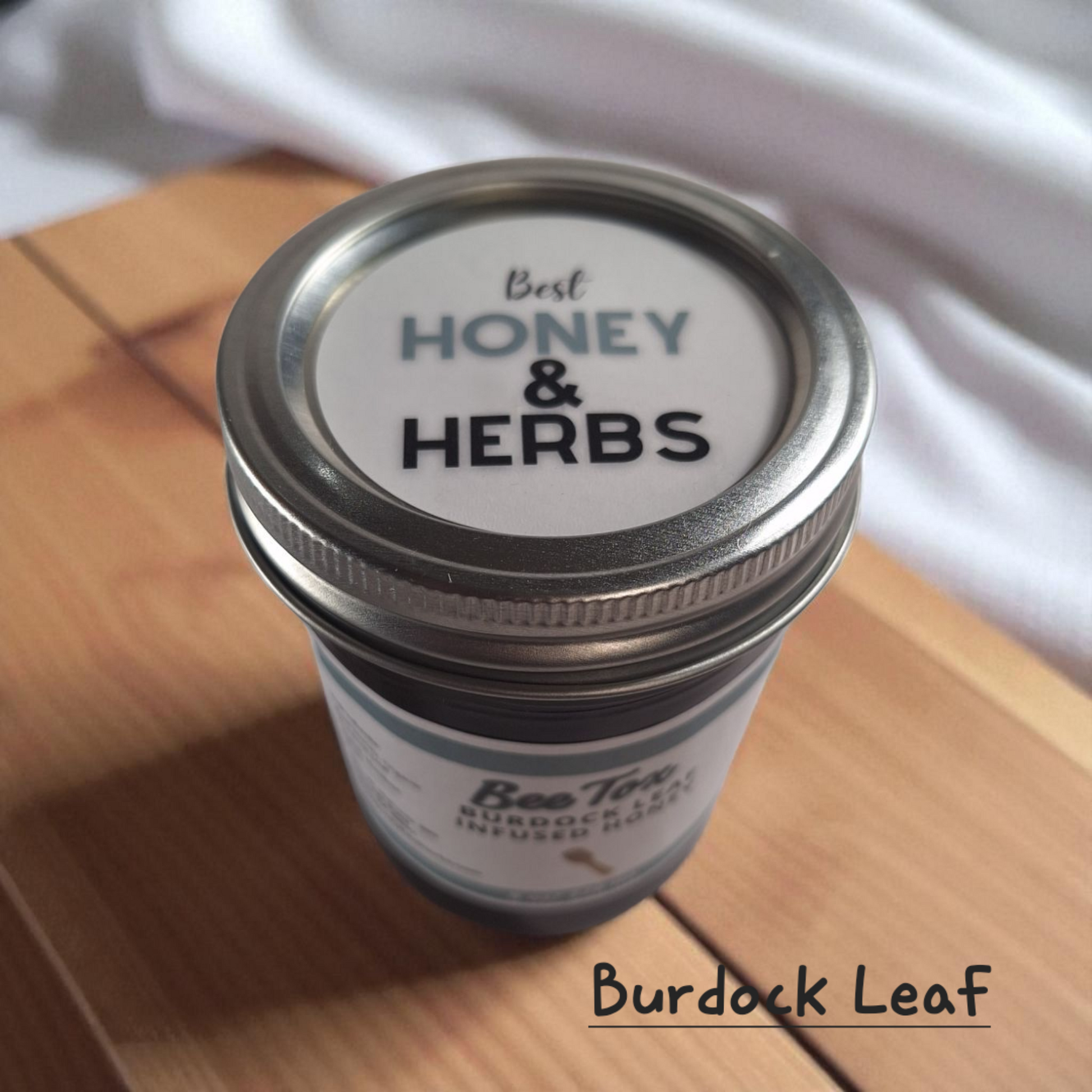 Top view of 8 oz half-pint jar of raw Burdock Leaf Infused Honey on a rustic wooden surface, herbal sweetener for detox teas, tonics, and healthy recipes.