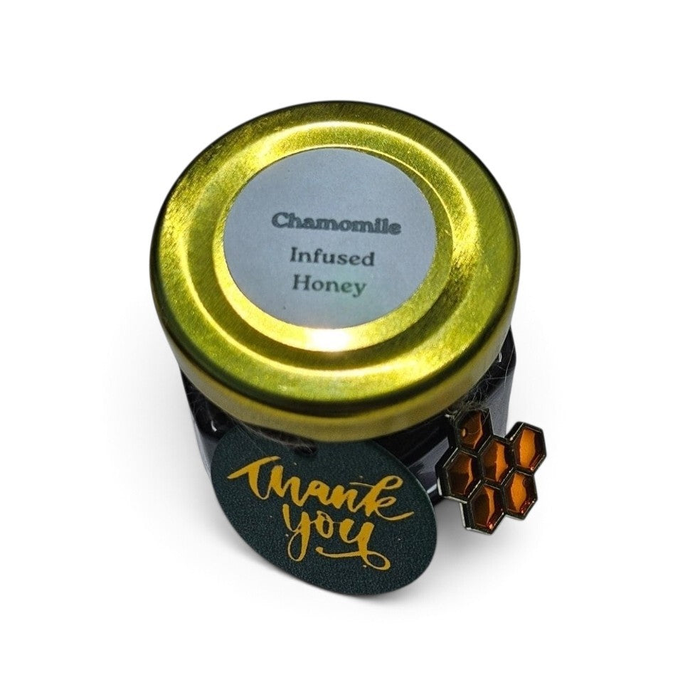 A small jar of Chamomile Infused Honey with a shiny gold lid and a green tag that says 'thank you' in gold script, shown on a white background.