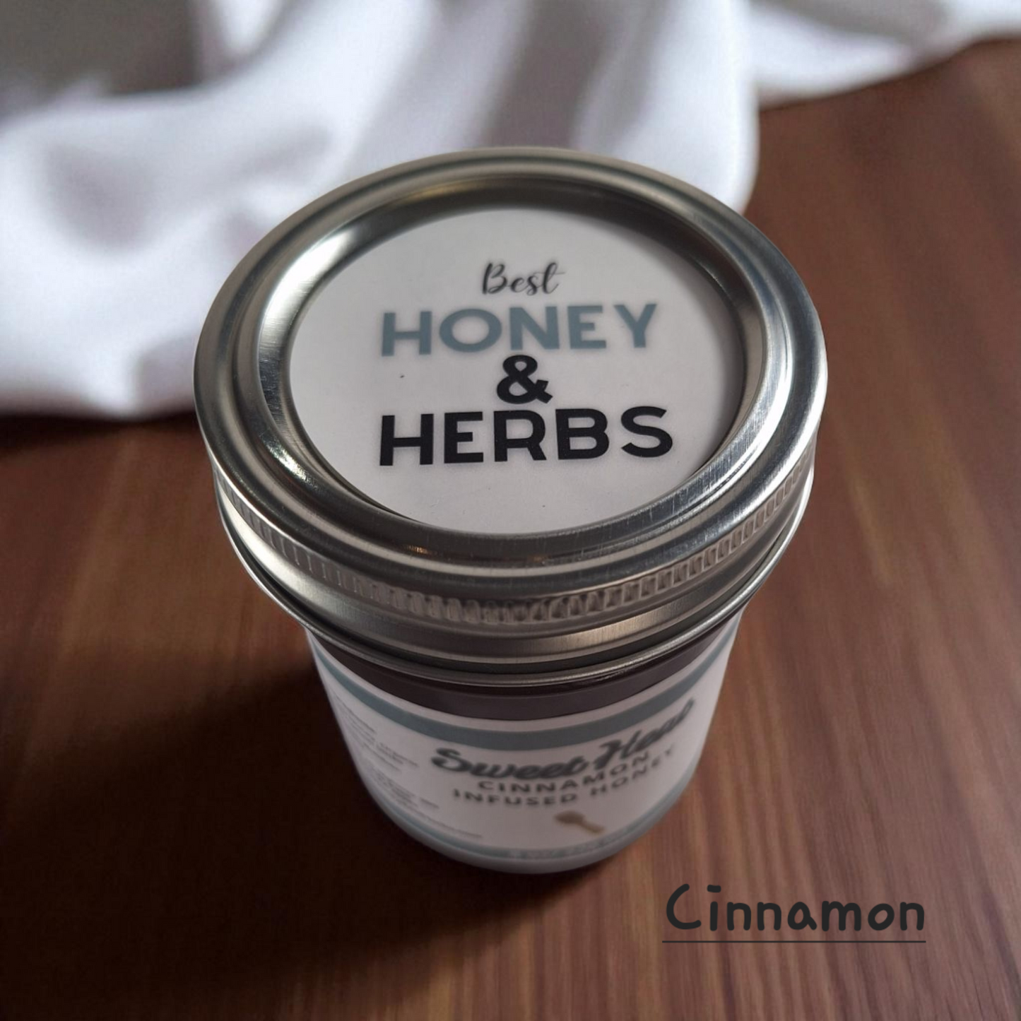 Overhead close-up of an 8 oz Cinnamon Infused Honey jar on dark wood grain; warm spiced sweetener for apple crisps, oatmeal, and coffee drinks.
