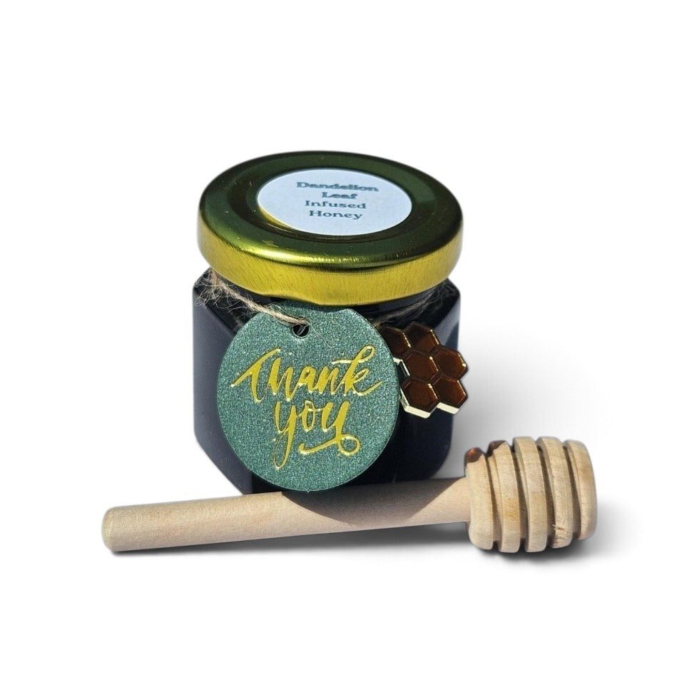 A small jar of Dandelion Leaf honey with a gold lid and a round green 'thank you' tag, shown with a wooden honey dipper on a white background.