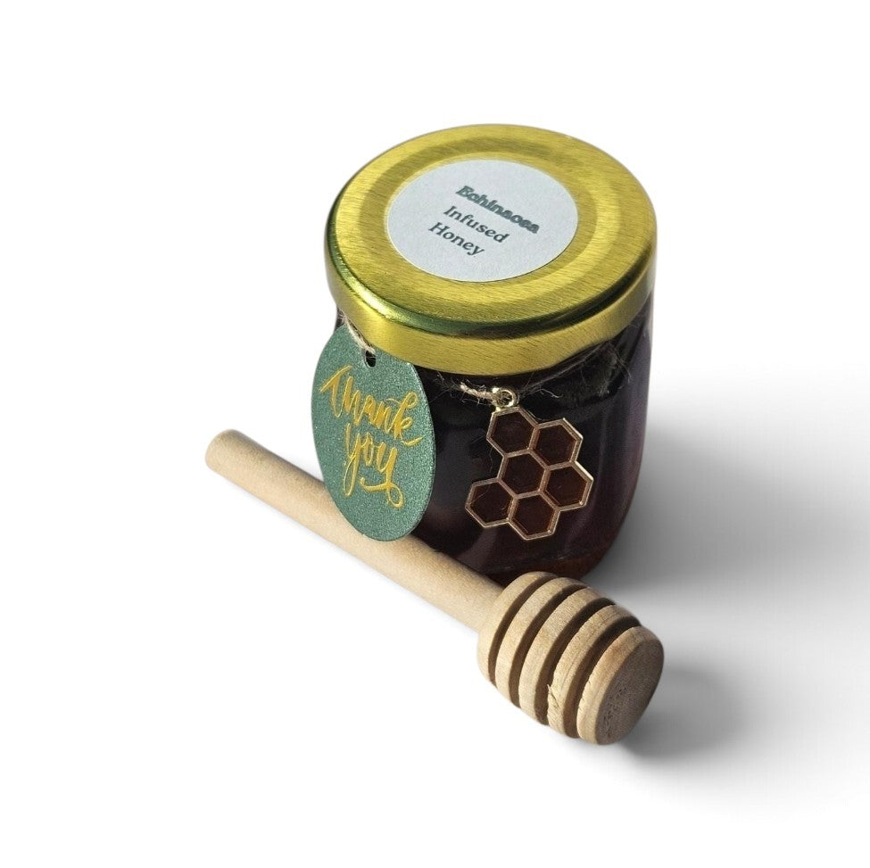 A small glass jar of honey with a gold lid and a round white label reading 'Echinacea Infused Honey,' shown on a white background with a wooden honey dipper and a green hang tag that says 'thank you.'.