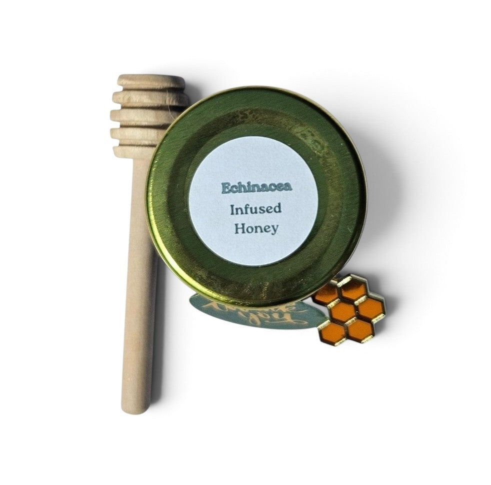 A top down view of Echinacea Infused Honey sample with a wooden honey dipper and a small honeycomb-shaped accent on a white background.