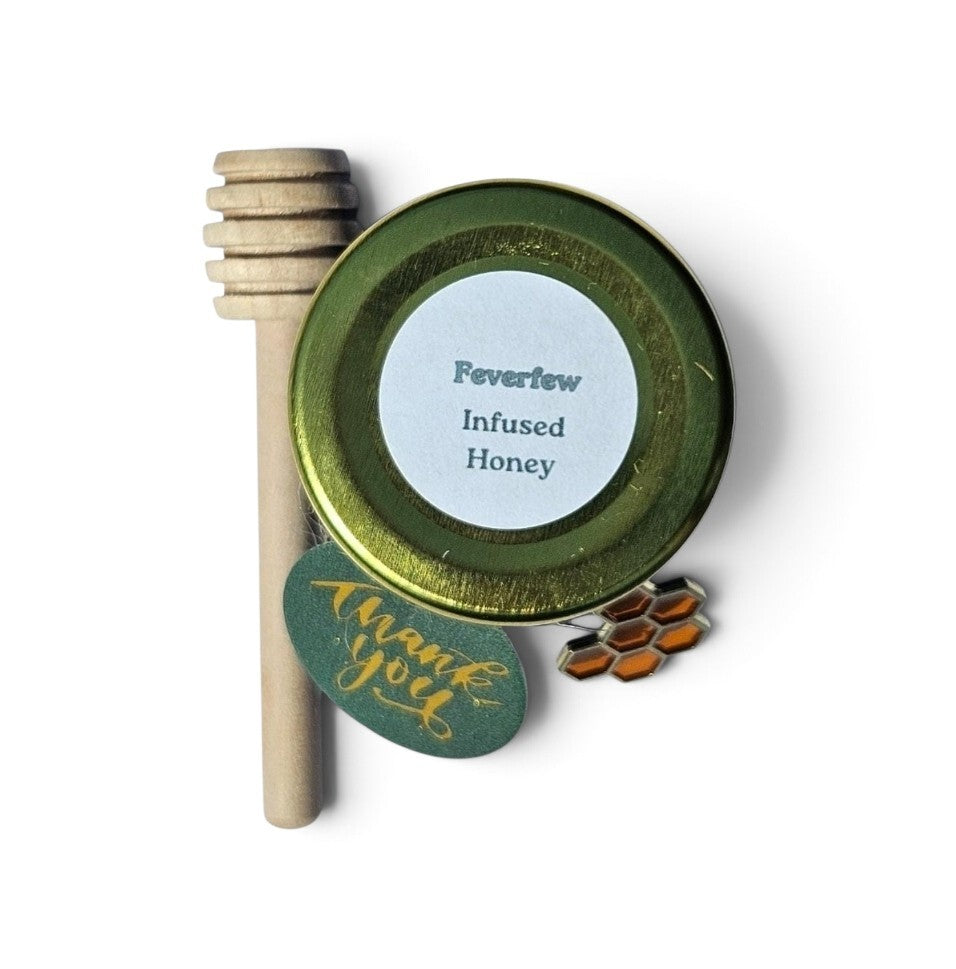 A small round jar of Feverlew Infused Honey with a wooden honey dipper and a green round tag reading 'thank you' on a white background.