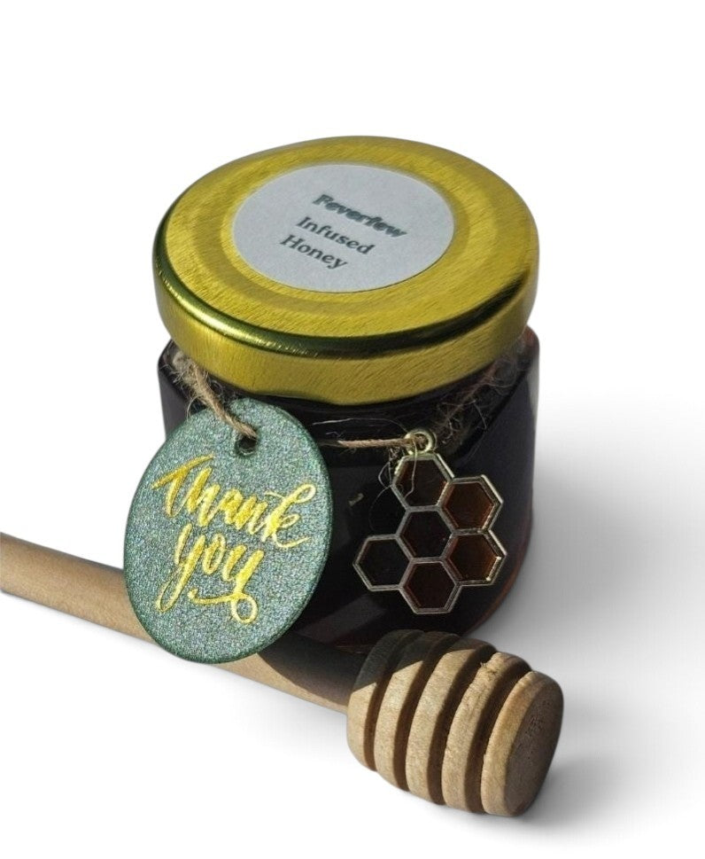 A jar of Perleview Infused Honey with a gold lid, a wooden honey dipper, and a glittery green 'thank you' tag on a white background.