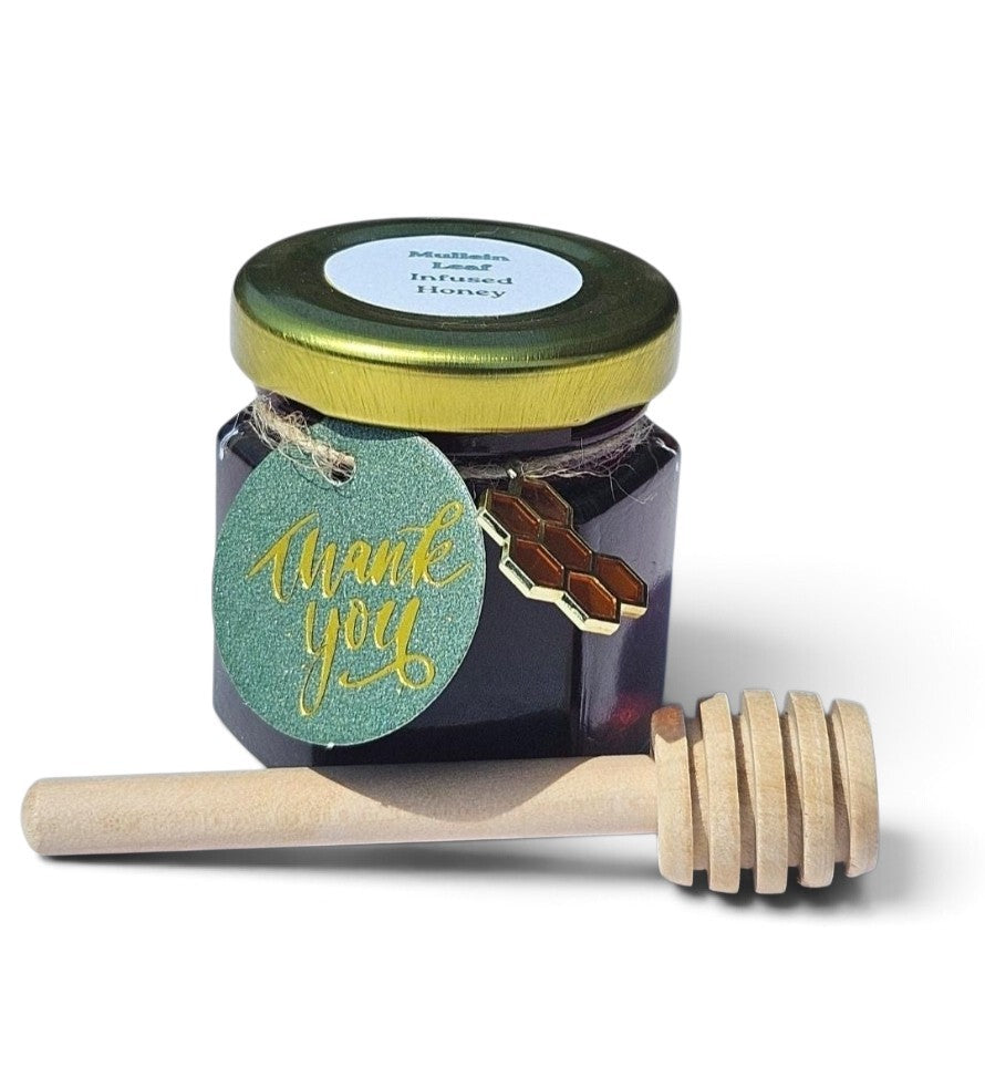 A sample jar of dark honey with a gold lid and a green 'thank you' tag, shown with a wooden honey dipper on a white background.