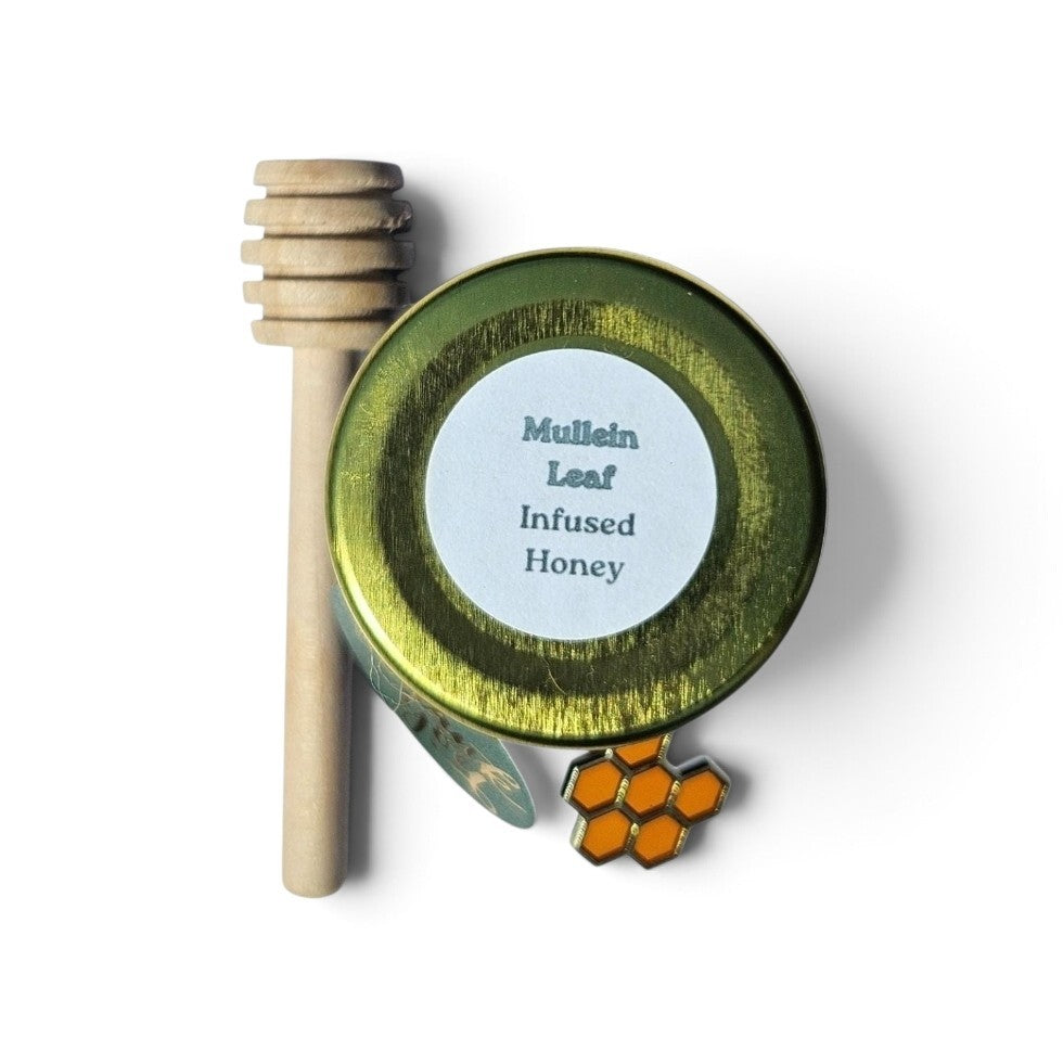 A jar of infused honey with a wooden honey dipper and a small honeycomb-shaped accessory on a white background. The round jar has a gold lid with a white label reading 'Mullein Leaf Infused Honey'.