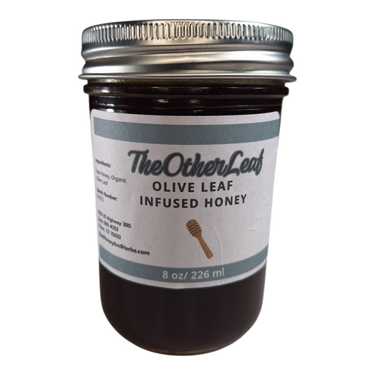 8 oz jar of raw Olive Leaf Infused Honey, herbal sweetener for tea, wellness tonics, and healthy recipes, on a plain white background.