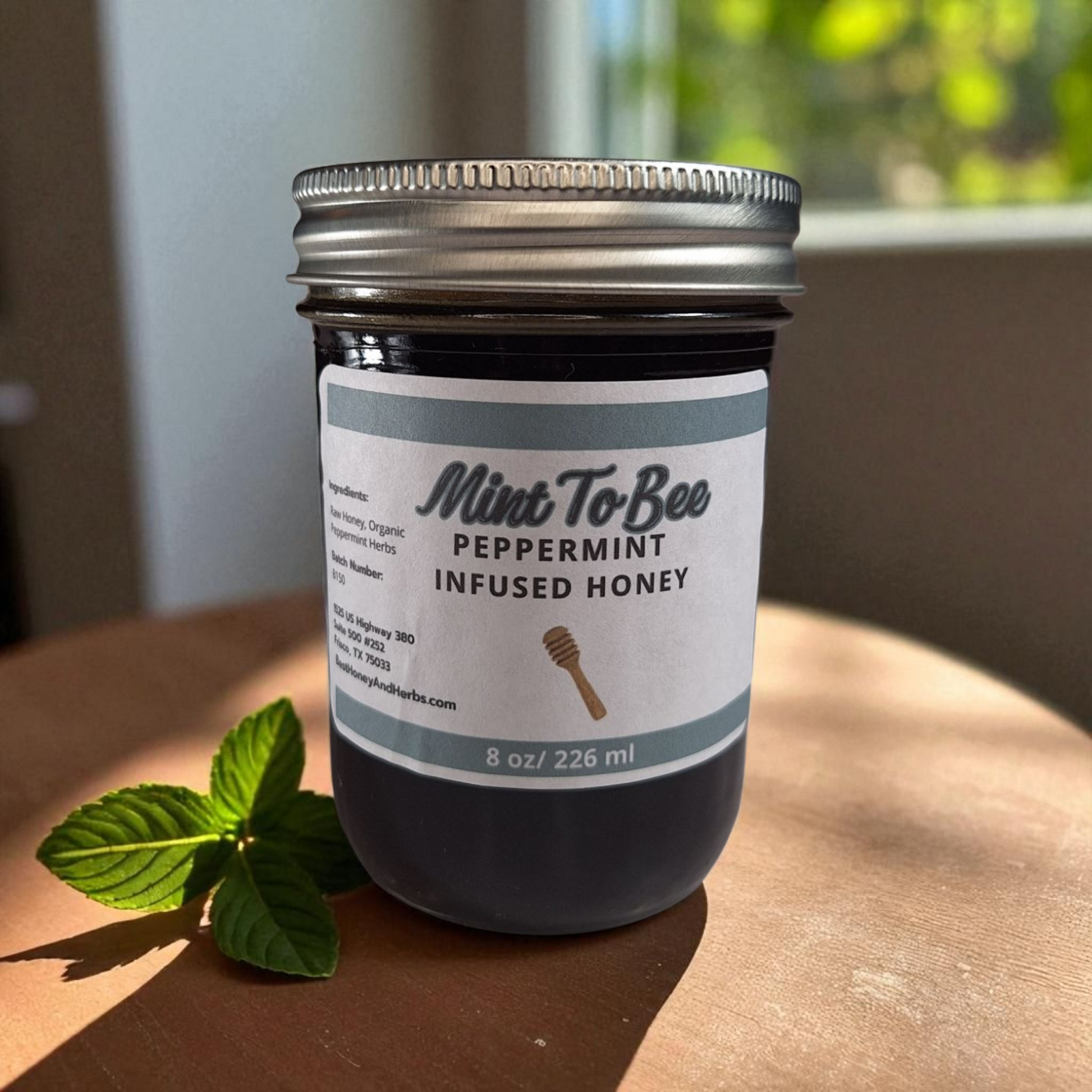 8 oz half-pint jar of raw Peppermint Leaf Infused Honey on a wooden surface, refreshing herbal sweetener for tea, baking, and holiday treats.