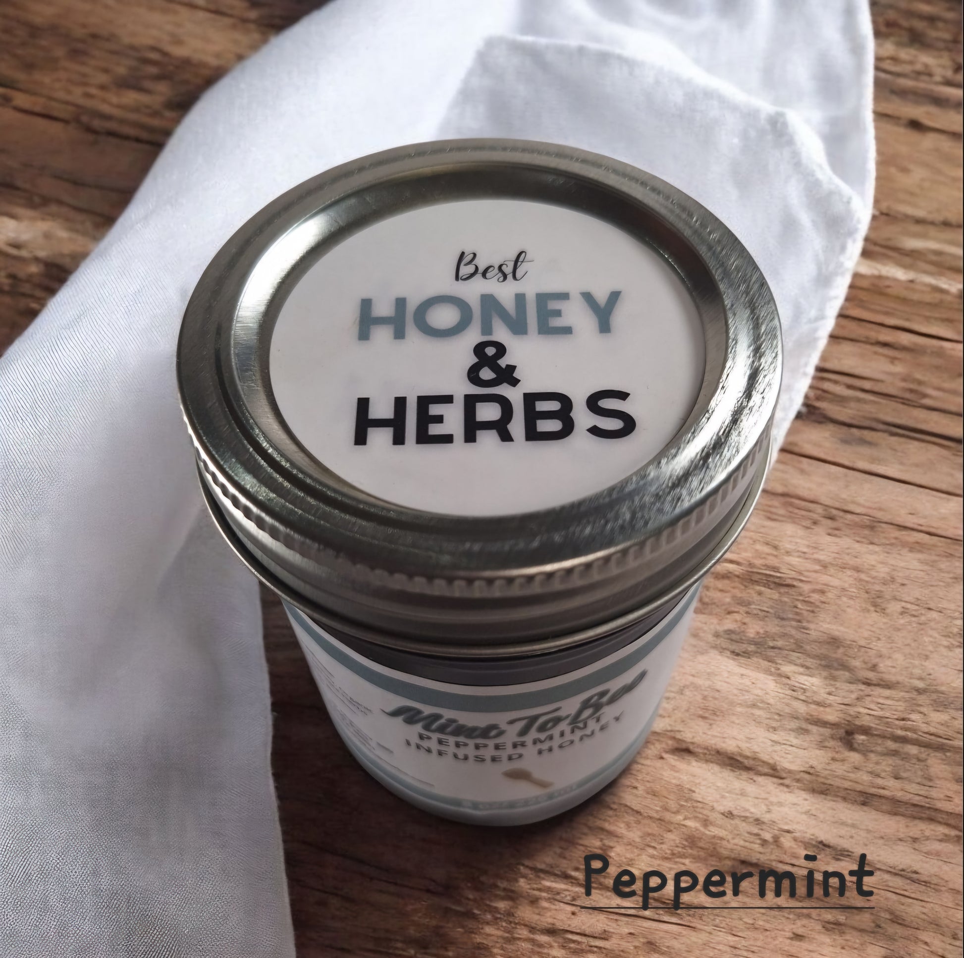 Top view of 8 oz half-pint jar of raw Peppermint Leaf Infused Honey on a wooden surface, refreshing herbal sweetener for tea, baking, and holiday treats.