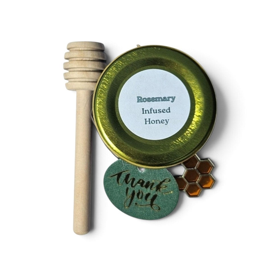 A sample jar of Rosemary Infused Honey in a round metal tin with a wooden honey dipper, a green round tag reading 'Thank You', and a small honeycomb charm on a white background.