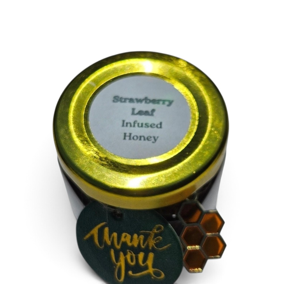 A 1.5 oz jar of Strawberry Leaf Infused Honey with a shiny gold lid and a dark green round tag that reads 'Thank you' in gold script, shown on a white background.