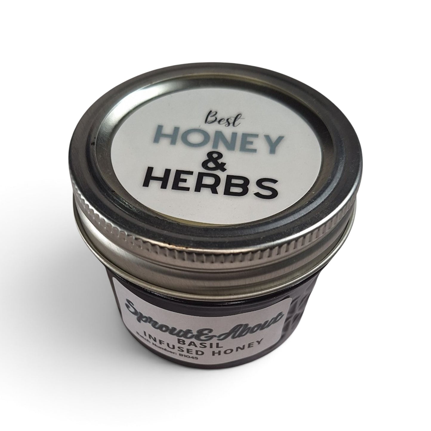 Basil infused raw honey in a small glass jar with a metal lid, top-down view.