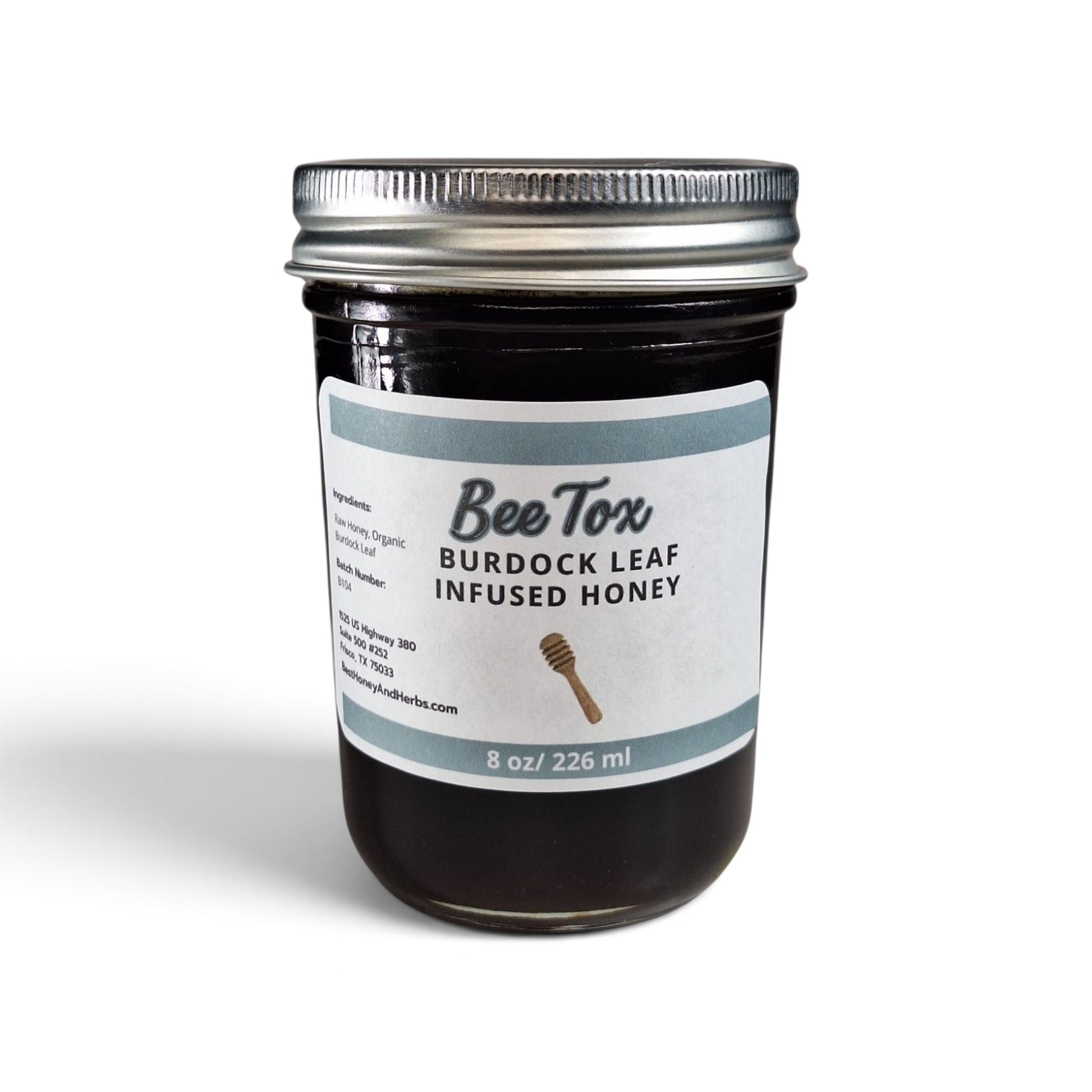 Burdock leaf infused raw honey in a glass jar with a silver metal lid.