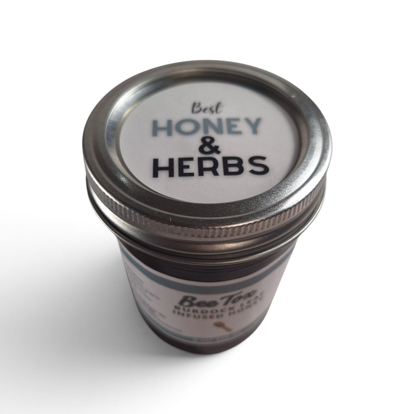 Burdock leaf infused raw honey in a glass jar with a silver metal lid.