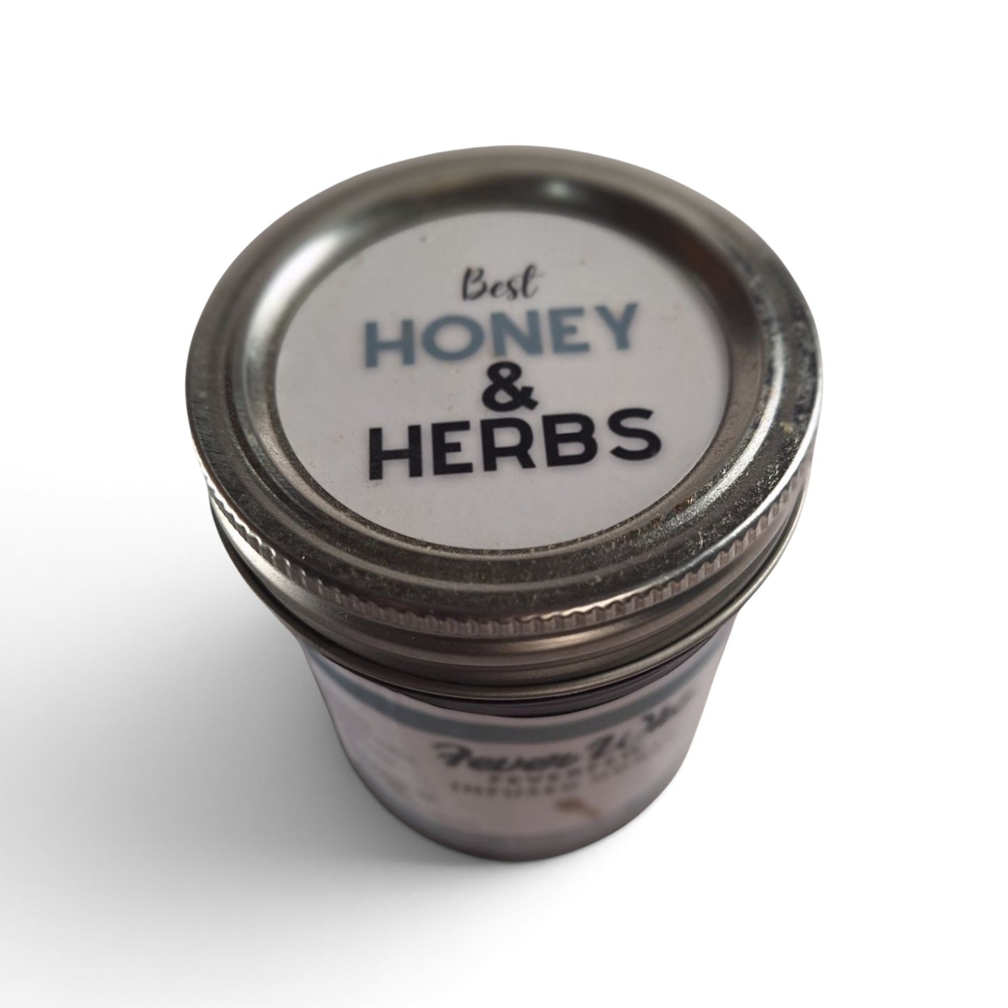  Feverfew infused raw honey in a small glass jar with a metal lid, top-down view.