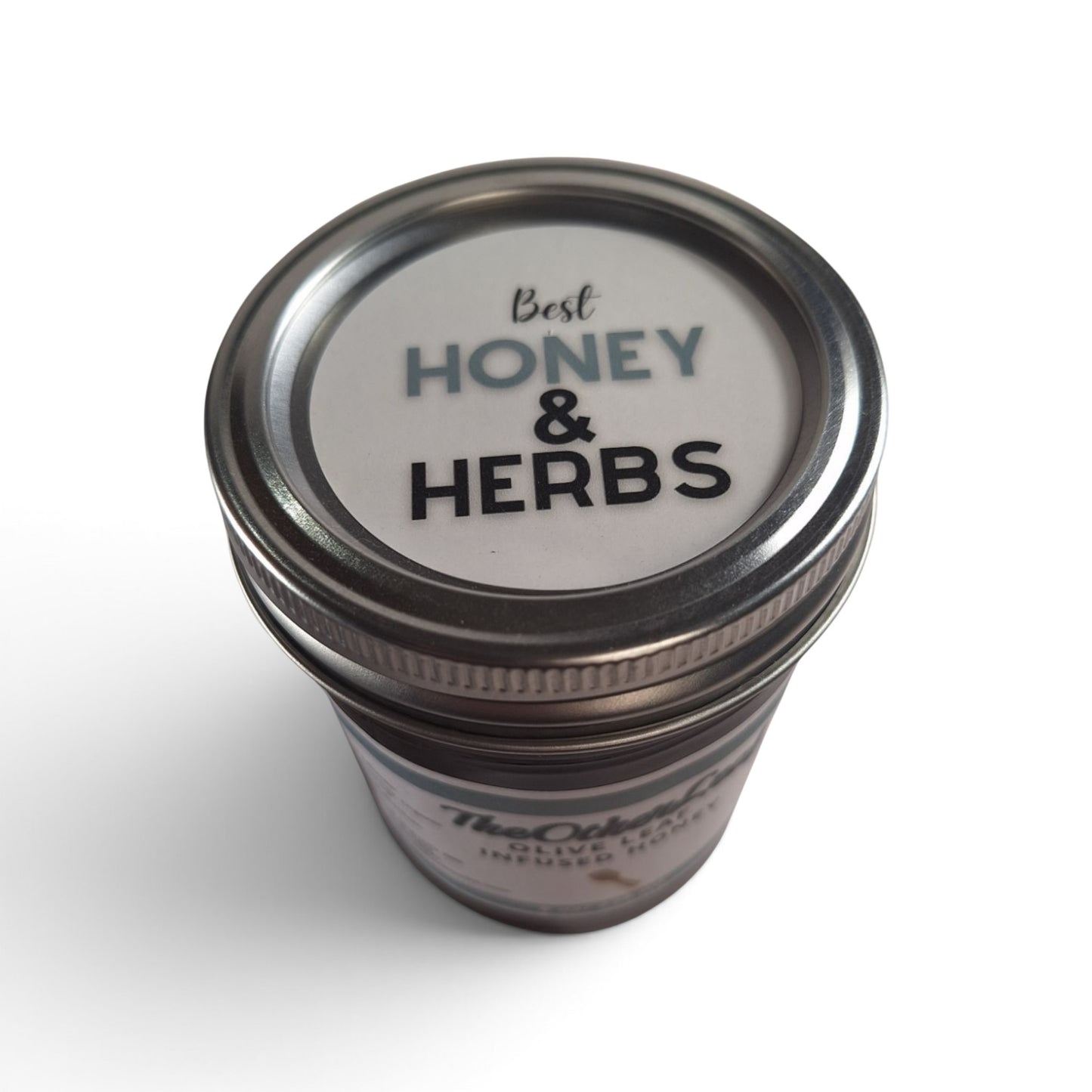 Olive leaf infused raw honey seen from a top-down angle with a metallic lid.