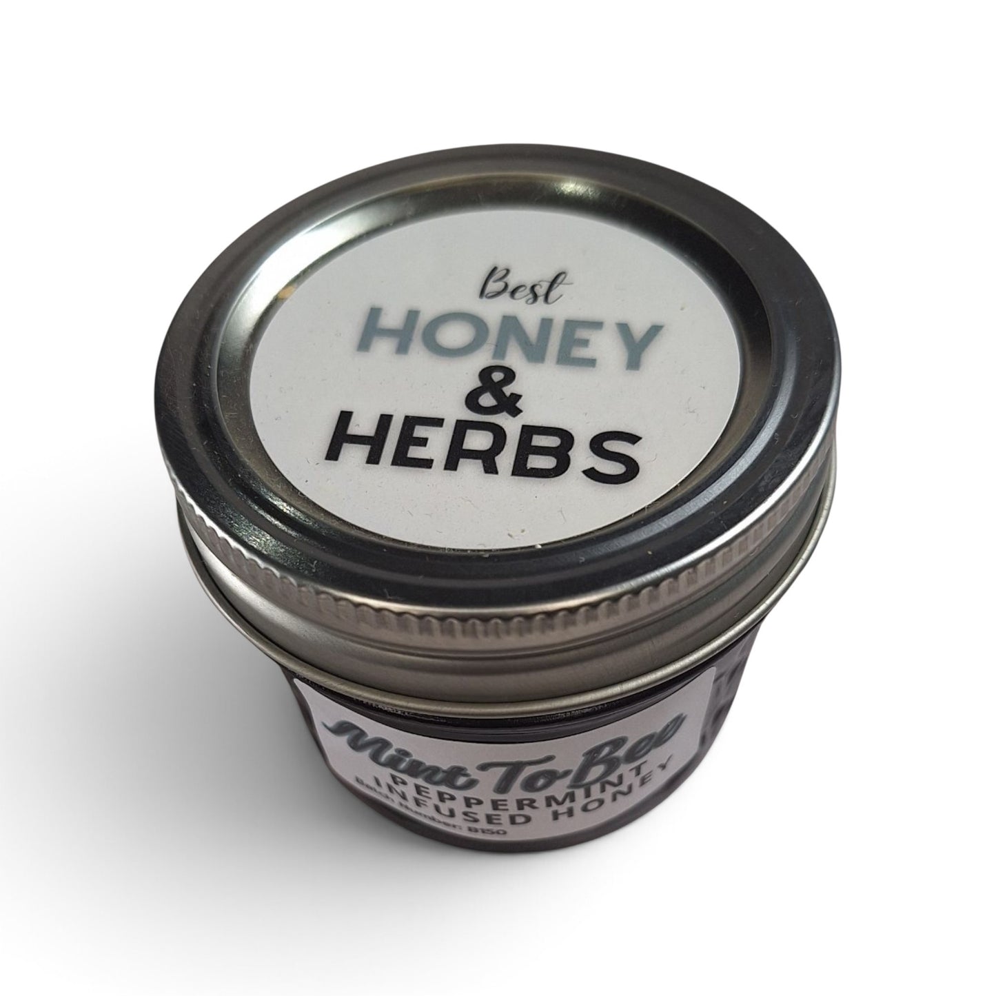  Peppermint infused raw honey in a small glass jar with a silver metal lid. 