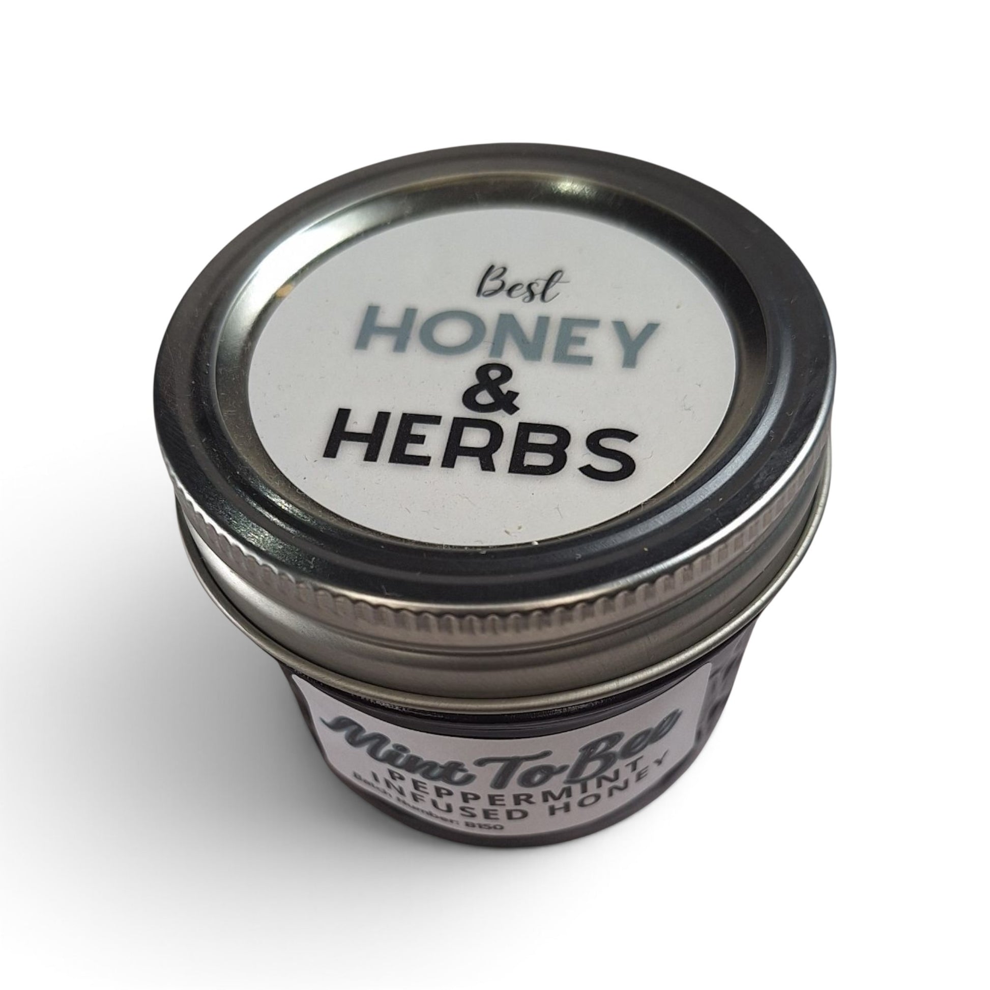  Peppermint infused raw honey in a small glass jar with a silver metal lid. 
