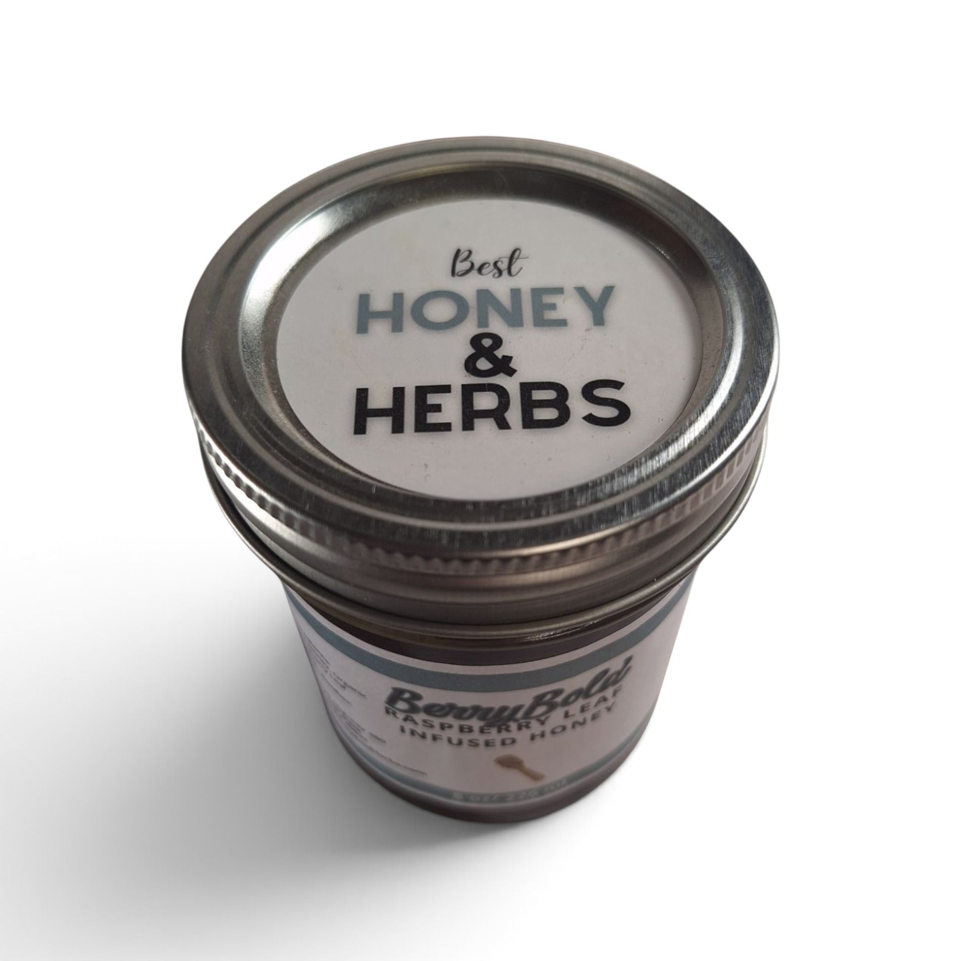  Raspberry leaf infused honey in a glass jar with a metal lid, top-down view.