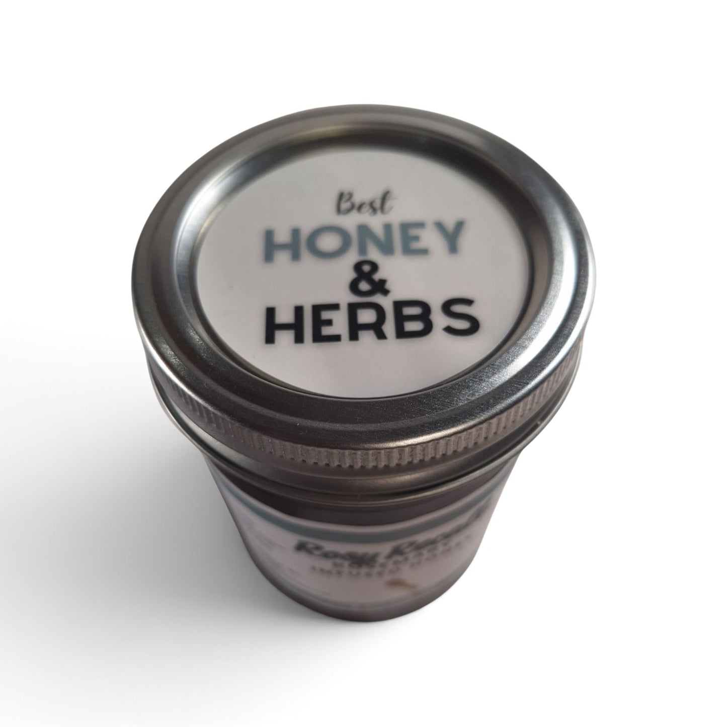  Rosemary infused raw honey in a glass jar with a silver metal lid, top-down view.
