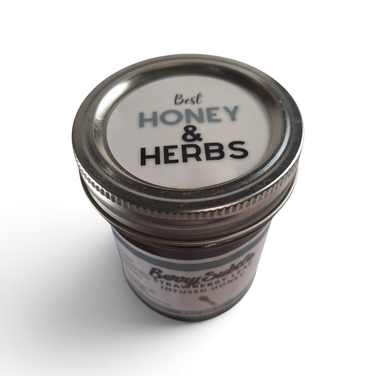  Strawberry leaf infused raw honey in a glass jar with a metal lid, top-down view.