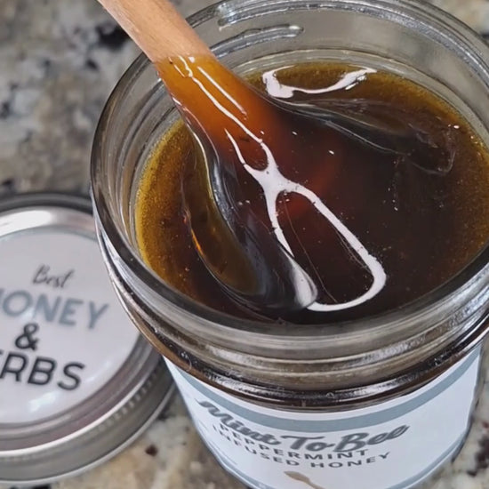 Peppermint leaf infused honey slowly drizzling from a honey dipper.