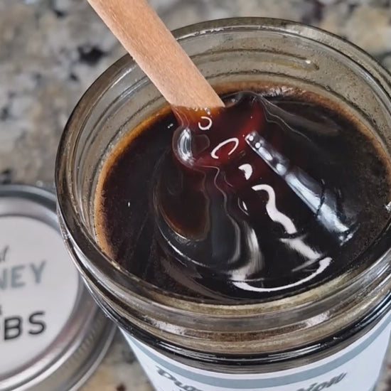 Elderberry infused honey slowly drizzling from a honey dipper.