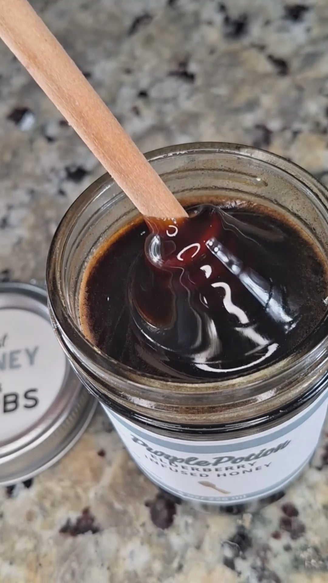 Elderberry infused honey slowly drizzling from a honey dipper.