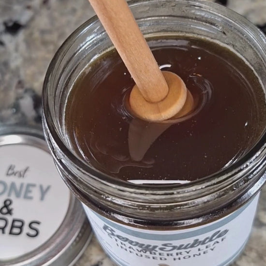  Strawberry leaf infused honey slowly drizzling from a honey dipper.