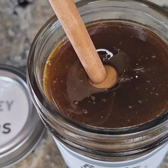  Burdock leaf infused honey slowly drizzling from a honey dipper.