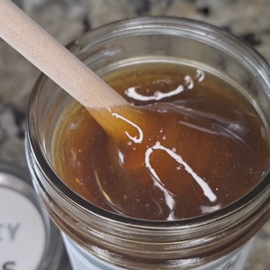  Raspberry Leaf infused honey slowly drizzling from a honey dipper.