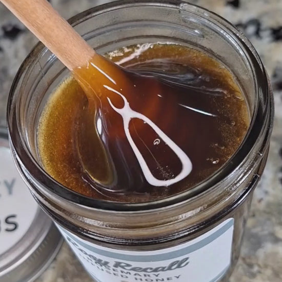Rosemary infused honey slowly drizzling from a honey dipper.