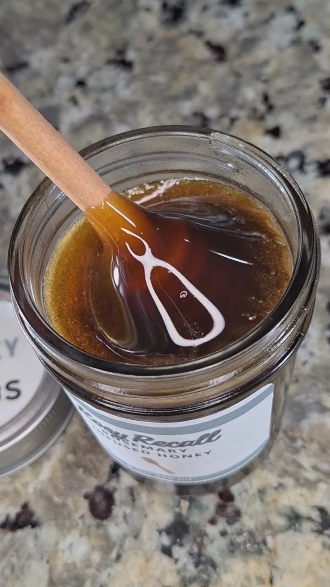 Rosemary infused honey slowly drizzling from a honey dipper.