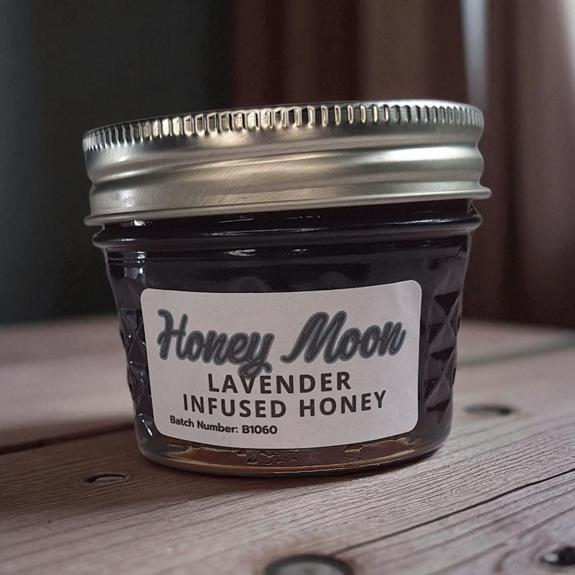 4 oz jar of raw Lavender Infused Honey on a rustic wooden surface, floral herbal sweetener for tea, baking, and relaxing drinks.
