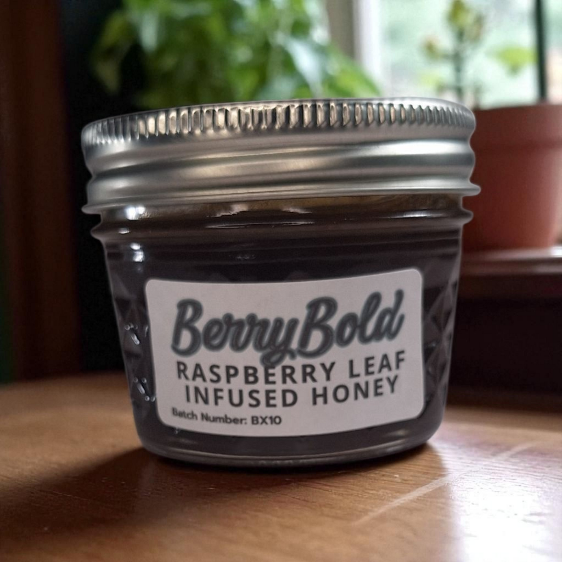 4 oz jar of raw Raspberry Infused Honey on a rustic wooden surface, fruity herbal sweetener for tea, desserts, and baking.
