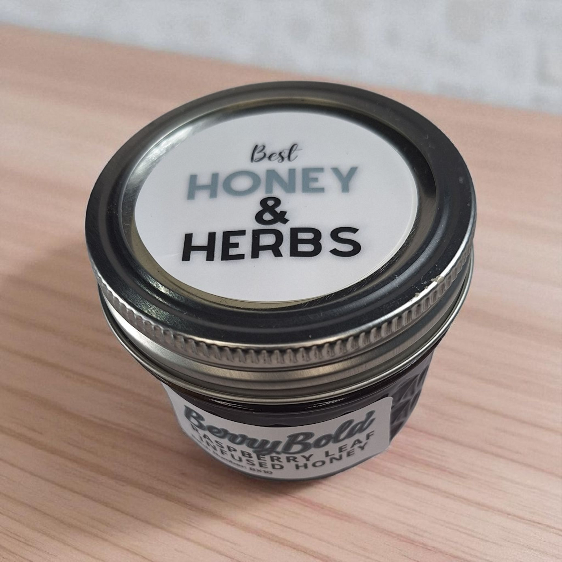 Flat-lay 4 oz Raspberry Infused Honey on a wood surface; bright, fruity herbal honey for yogurt, pancakes, and desserts.
