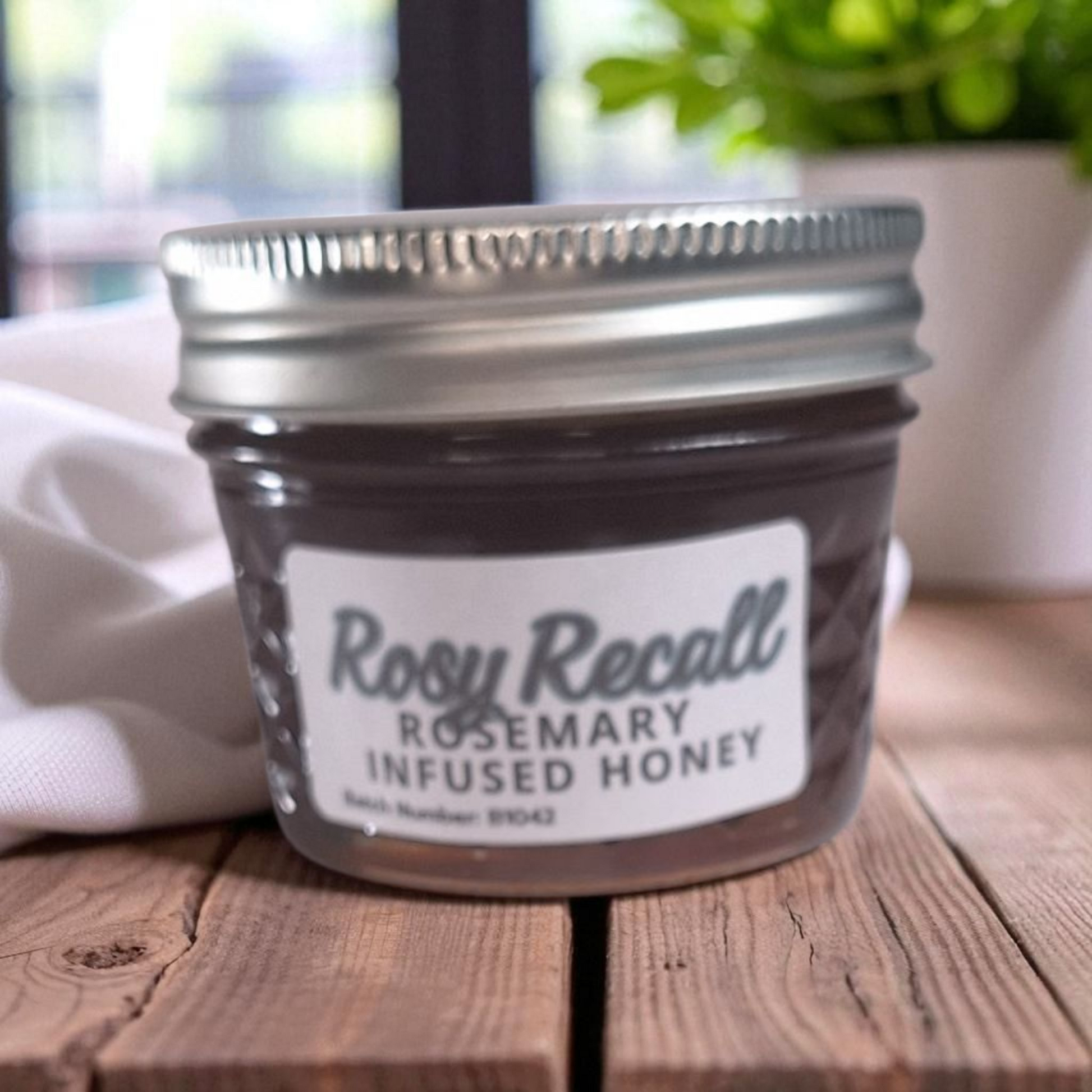 4 oz jar of raw Rosemary Infused Honey on a wooden surface, savory herbal sweetener for meats, bread, and roasted vegetables.