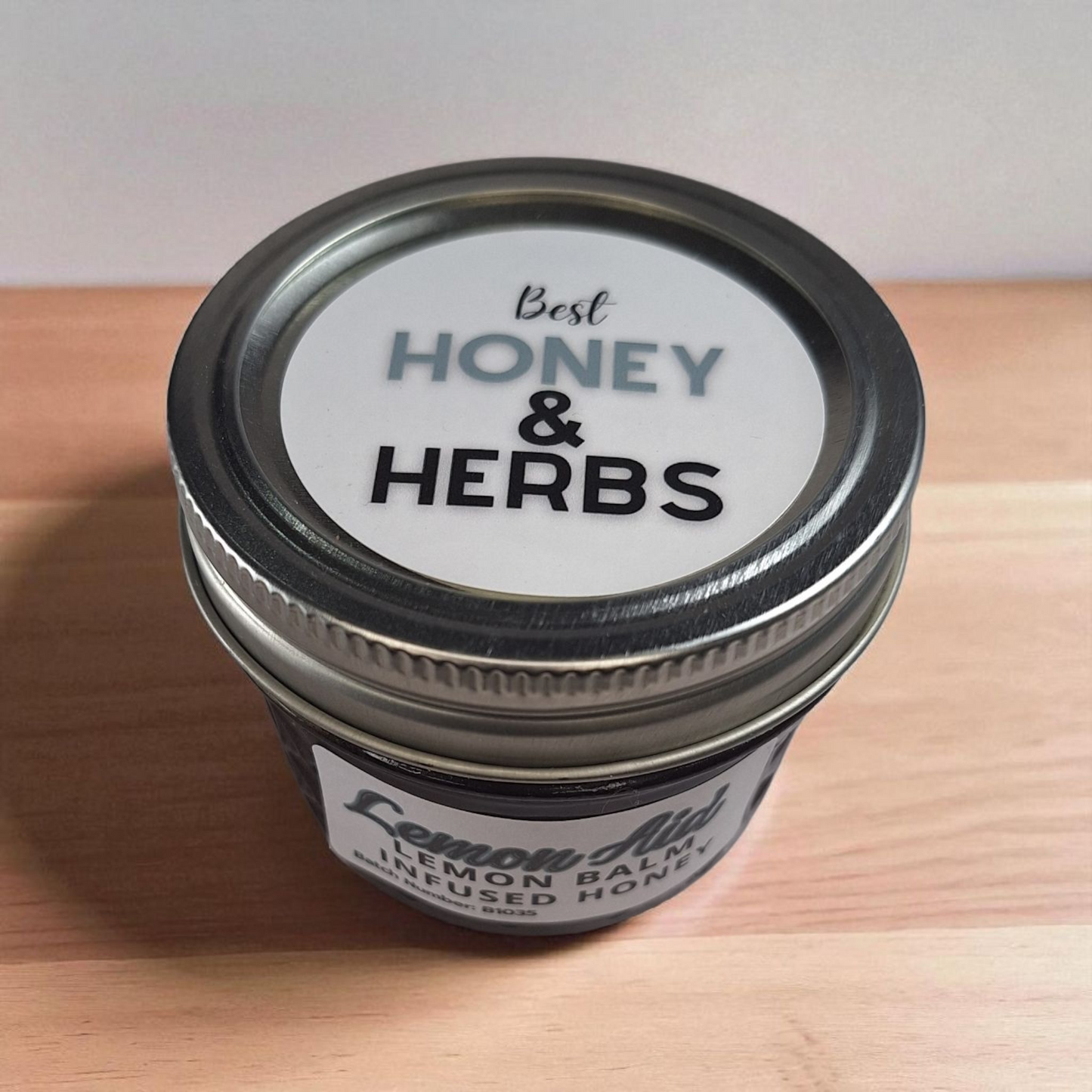 Overhead 4 oz Lemon Balm Infused Honey on light wood; citrusy herbal honey for iced tea, vinaigrettes, and cakes.
