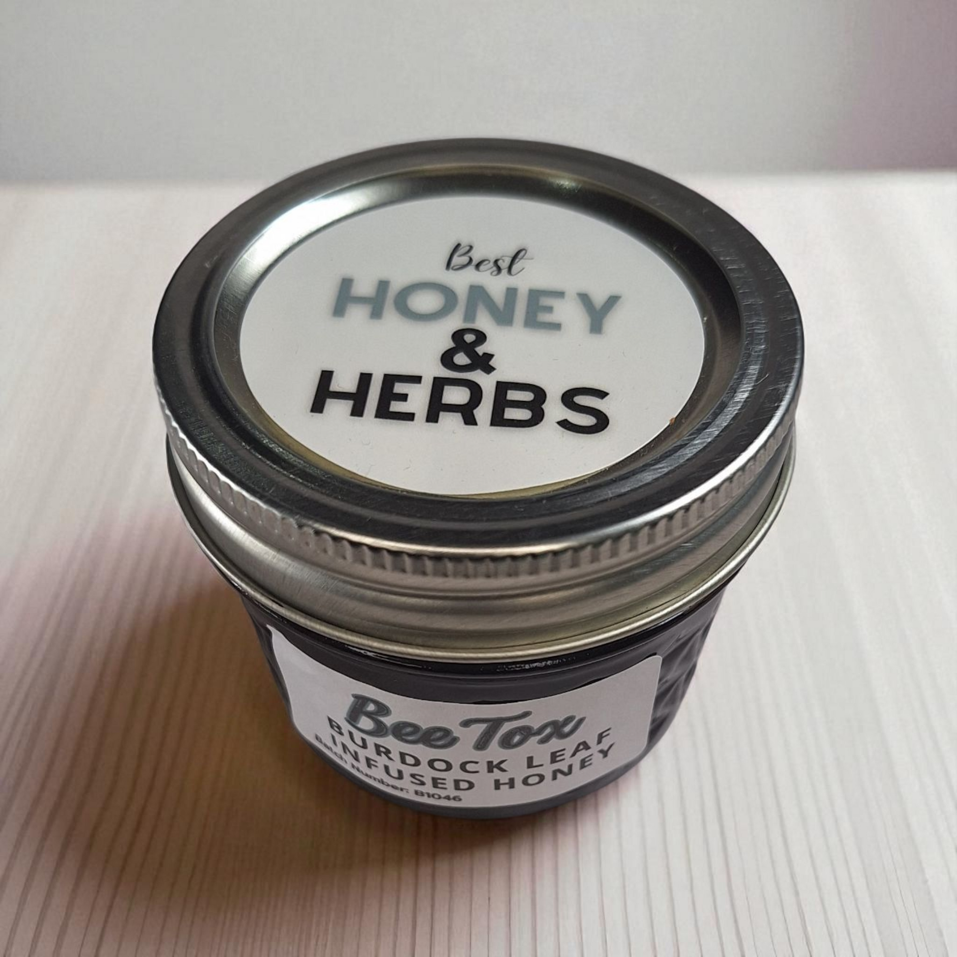 Bird’s-eye view of a 4 oz jar of Burdock Leaf Infused Honey on rustic wood; small-batch herbal sweetener for earthy teas and tonics.
